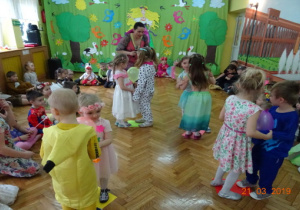Dzieci w wiosennych przebraniach na tle dekoracji tańczą w parach z balonem.